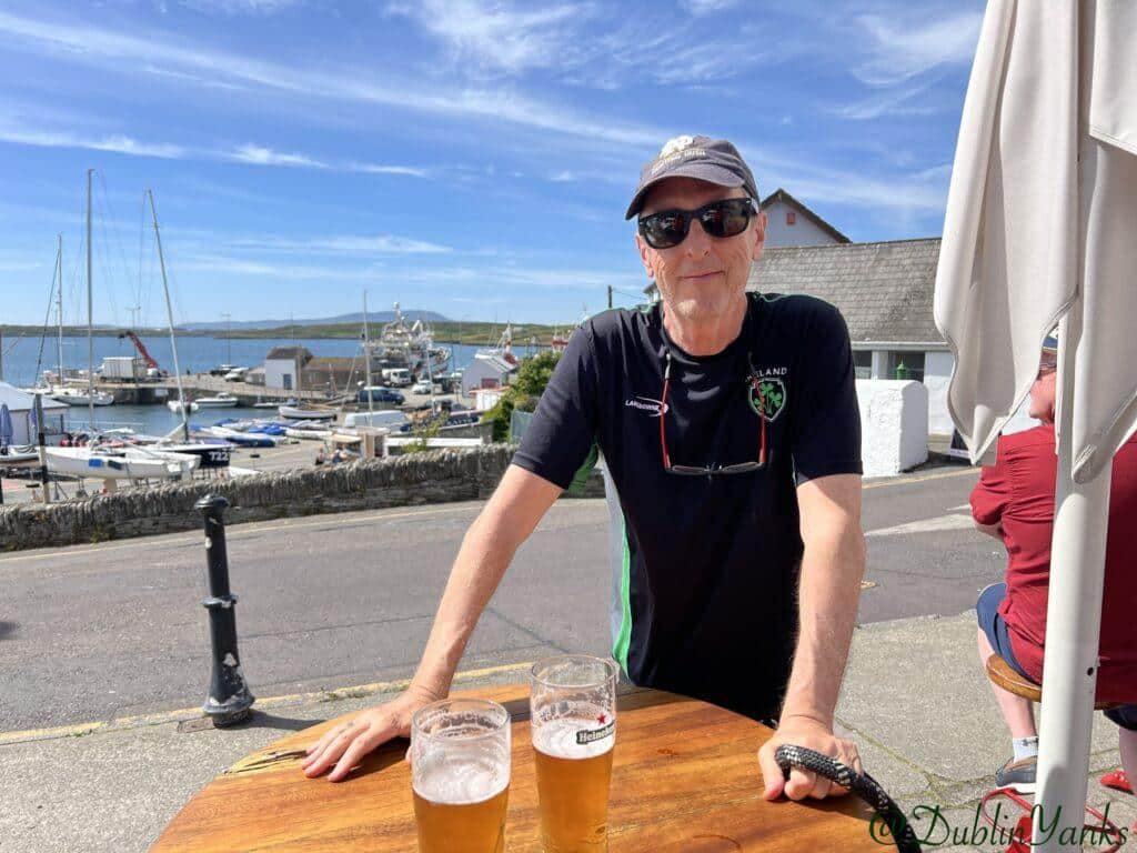 Marina at Baltimore in County Cork A man, standing at a table with 2 pints of beer on a summer day in front of a marina